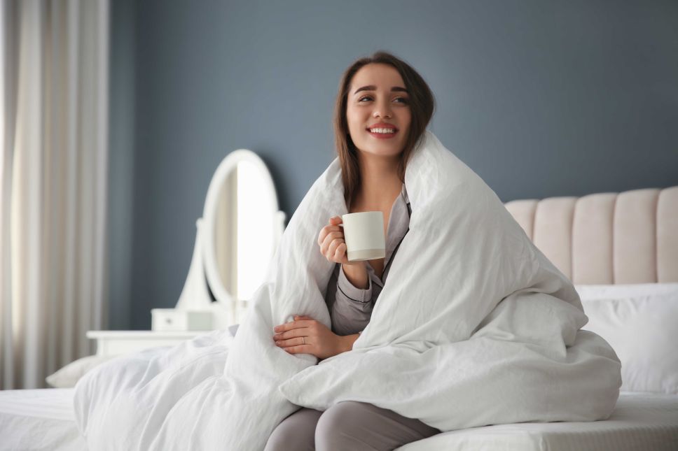 a woman sitting up her bed covered in a blanket